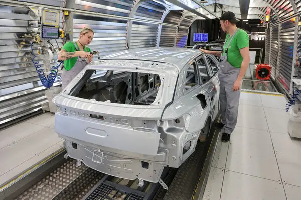 Partially assembled silver car body positioned on a factory assembly line.